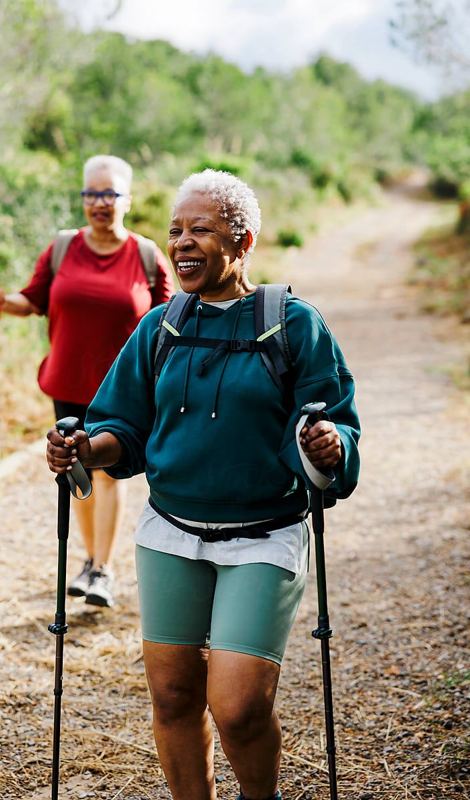 Two women in their 40s and 50s trekking-pole hiking together, smiling
