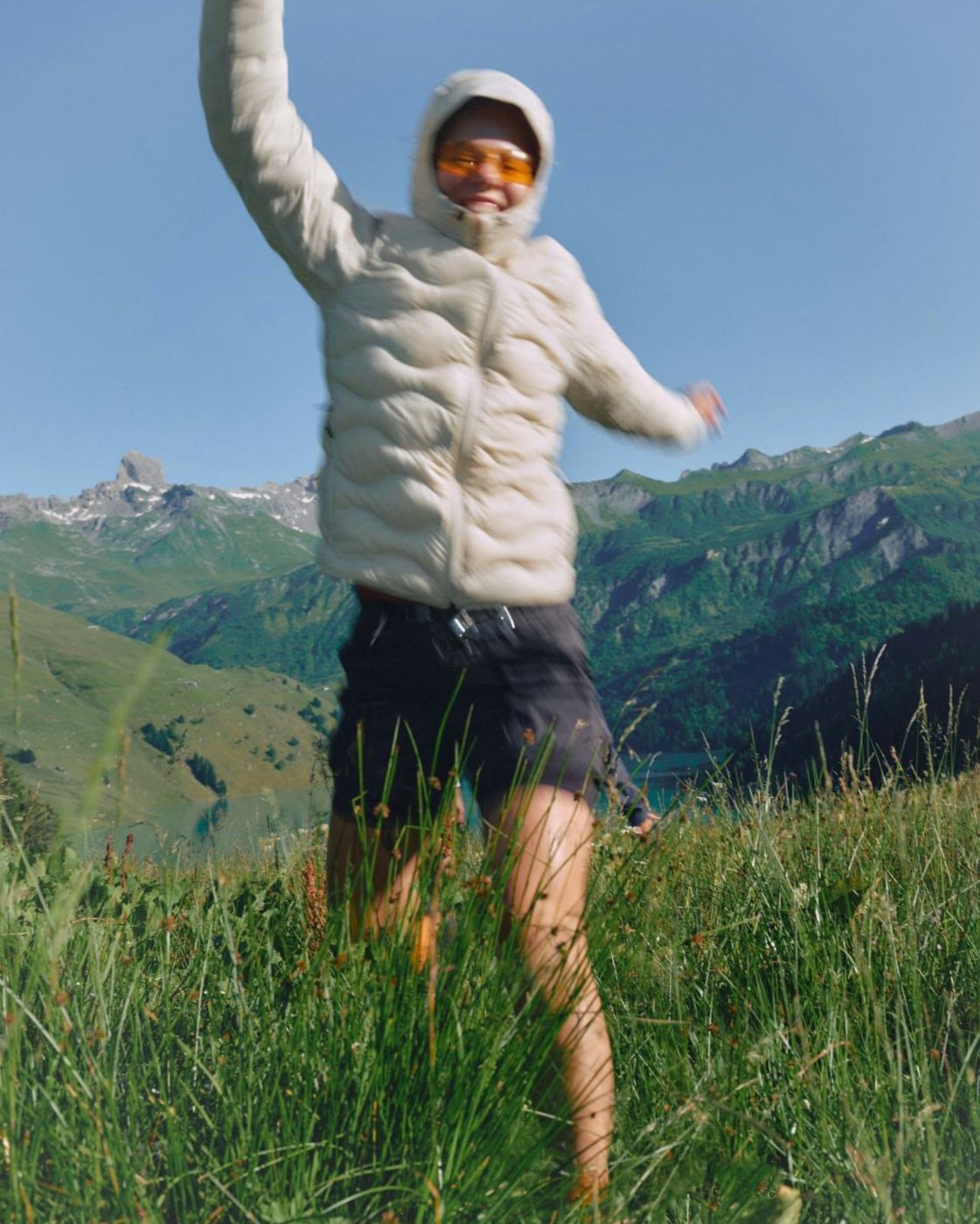 Woman jumping mid-stride in an alpine meadow, mountains behind her
